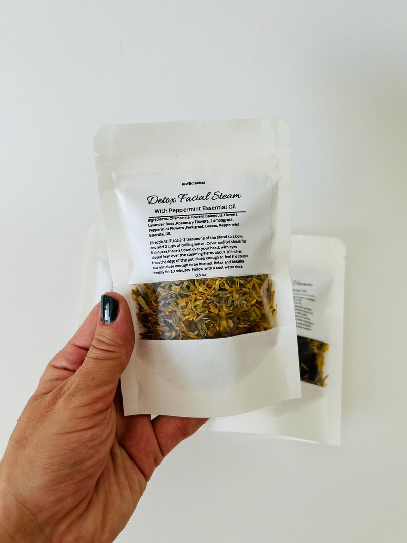 May include: A white pouch with a clear window showing a blend of dried herbs and flowers. The pouch is labeled "Detox Facial Steam with Peppermint Essential Oil". The ingredients are listed as chamomile flowers, calendula flowers, lavender buds, rosemary flowers, lemongrass, peppermint flowers, fenugreek leaves, and peppermint essential oil. The directions are to place 2-3 teaspoons of the blend in a bowl with 3 cups of boiling water, cover and let steam for 5 minutes. Place a towel over your head, with eyes closed, lean over the steaming herbs about 10 inches from the edge of the pot, close enough to feel the steam but not close enough to be burned. Relax deeply for 10 minutes. Follow with a cool water rinse. 0.5 oz.