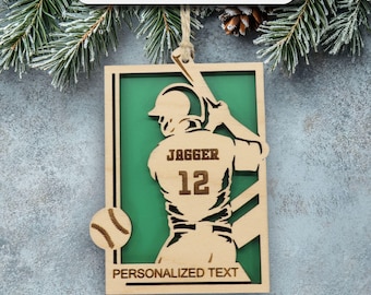 May include: Wooden baseball ornament with a green background. The ornament features a baseball player silhouette with the name "JAGGER" and the number "12". The text "PERSONALIZED TEXT" is at the bottom. A baseball is on the left side. The top text says "BUY 2+ SAVE 20-40%".
