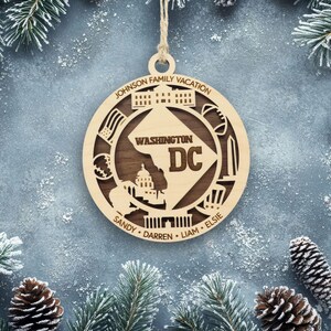 May include: A circular wooden ornament featuring a cutout map of Washington DC with the text 'WASHINGTON DC' and 'JOHNSON FAMILY VACATION'. The design includes icons of the White House, Capitol, and Washington Monument, with names Sandy, Darren, Liam, and Elsie.