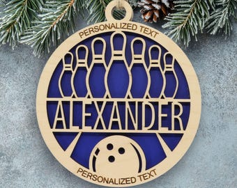 May include: A circular wooden ornament featuring a cutout design of seven bowling pins above the name ALEXANDER and a bowling ball at the bottom. The text PERSONALIZED TEXT is engraved at the top and bottom against a dark blue background.