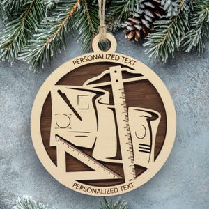 May include: A round wooden ornament featuring a layered design with a dark brown background and a light wood cutout overlay. The design depicts architectural drafting tools including a ruler, a triangle, and blueprints. The text PERSONALIZED TEXT is engraved at the top and bottom.
