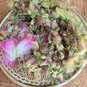 May include: A silver-colored, decorative tray filled with dried flowers and buds. The flowers are a mix of colors, including pink, purple, and yellow, with green stems. The tray sits on a wooden surface with a natural grain.