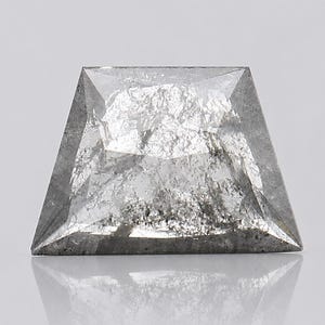 May include: A trapezoidal-shaped loose gemstone with a faceted surface. The stone features a translucent, salt-and-pepper appearance with a mix of clear, crystalline sections and dark, speckled inclusions throughout its internal structure.