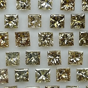May include: A collection of 36 square-shaped, faceted, loose diamonds in various shades of yellow and brown. The diamonds are arranged in a symmetrical pattern on a white surface.