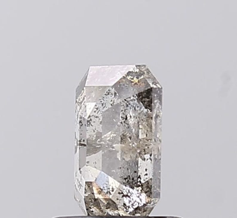 May include: A clear, grey rectangular-cut gemstone with internal inclusions. The gem has a polished surface with multiple facets, reflecting light. The overall shape is a tall, rectangular prism, showcasing the stone's clarity and unique characteristics.