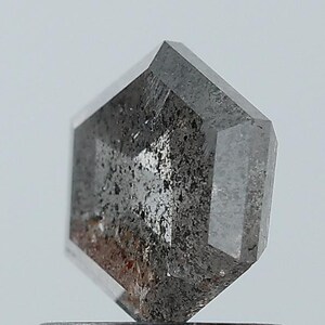 以下が含まれることがあります： ユニークな幾何学的な形状の、グレーの色合いのファセット宝石。石には濃いグレーと薄いグレーのインクルージョンが混在し、まだらの外観を作り出しています。ファセットは光を捉え、石の結晶構造を際立たせています。