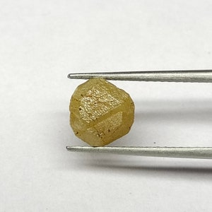 Pu&ograve; includere: Un diamante grezzo giallo sfaccettato tenuto da una pinza. Il diamante ha una finitura naturale non lucidata.