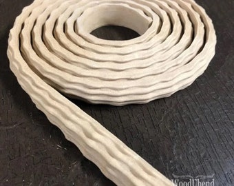 May include: A coiled, beige-colored, textured wood trim with a wavy pattern. The trim is rolled up, with a portion unrolled and extending towards the bottom left. The WoodUbend logo is visible in the bottom right corner.