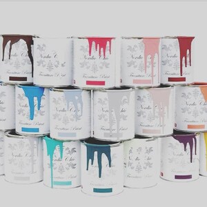 May include: A collection of paint cans in various colors, including teal, blue, gray, pink, red, and brown. The cans are labeled "Nordic Chic Furniture Paint".