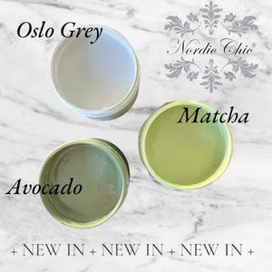 May include: Three paint samples in small jars. The colors are Oslo Grey, Avocado, and Matcha. The jars are on a white marble surface. The text "Nordic Chic" is in the background.