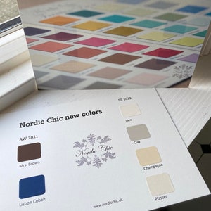 May include: A color chart with paint swatches for the brand Nordic Chic. The chart shows new colors for the Spring/Summer 2022 and Autumn/Winter 2021 seasons. The colors include Lace, Clay, Champagne, Plaster, Mrs. Brown, and Lisbon Cobalt.