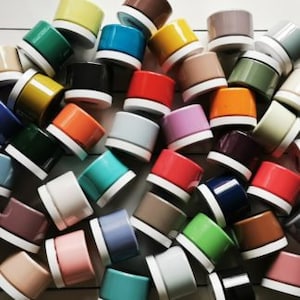 May include: A collection of colorful ceramic planters in various shades, including red, blue, green, yellow, and orange. The planters are all small and round, with a white rim.