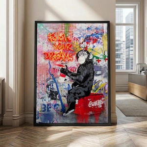 May include: Framed artwork depicting a chimpanzee with a spray can, sitting on a red Coca-Cola crate. The background is a vibrant graffiti design with the words "Follow Your Dreams".