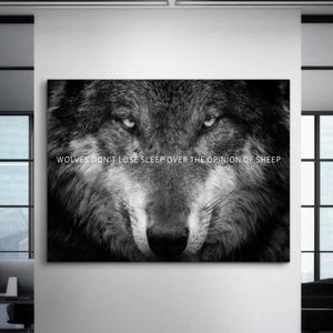 May include: A black and white wall art print featuring a close-up of a wolf's face with intense eyes and detailed fur texture. The text "WOLVES DON'T LOSE SLEEP OVER THE OPINION OF SHEEP" is printed in white capital letters across the center of the image.