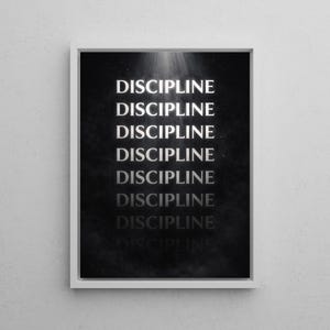 May include: A framed print with the word "DISCIPLINE" repeated vertically in a white, bold font against a dark, textured background. The print is in a white frame and is mounted on a white wall.
