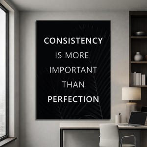 K&ouml;nnte beinhalten: Ein schwarz-wei&szlig;es Motivationsposter mit dem Text "CONSISTENCY IS MORE IMPORTANT THAN PERFECTION" in Wei&szlig;. Der Hintergrund zeigt ein dunkles, verschwommenes Bild von Palmenbl&auml;ttern. Das Kunstwerk wird in einem modernen B&uuml;roumfeld gezeigt.
