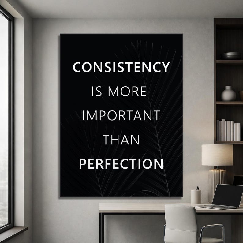 K&ouml;nnte beinhalten: Ein schwarz-wei&szlig;es Motivationsposter mit dem Text "CONSISTENCY IS MORE IMPORTANT THAN PERFECTION" in Wei&szlig;. Der Hintergrund zeigt ein dunkles, verschwommenes Bild von Palmenbl&auml;ttern. Das Kunstwerk wird in einem modernen B&uuml;roumfeld gezeigt.