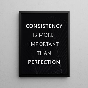 K&ouml;nnte beinhalten: Schwarz gerahmtes Wandbild mit dem wei&szlig;en Text "CONSISTENCY IS MORE IMPORTANT THAN PERFECTION". Der Hintergrund zeigt ein subtiles, dunkles Blattmuster. Das Kunstwerk wird vor einer hellgrauen Wand pr&auml;sentiert.