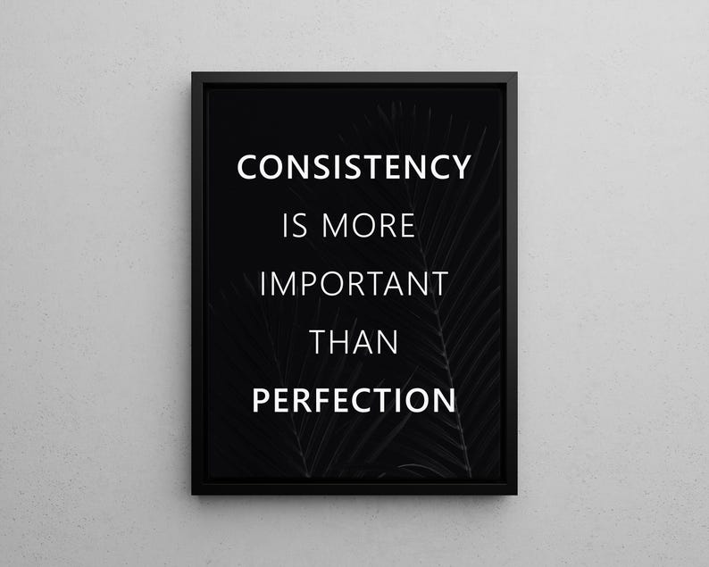 K&ouml;nnte beinhalten: Schwarz gerahmtes Wandbild mit dem wei&szlig;en Text "CONSISTENCY IS MORE IMPORTANT THAN PERFECTION". Der Hintergrund zeigt ein subtiles, dunkles Blattmuster. Das Kunstwerk wird vor einer hellgrauen Wand pr&auml;sentiert.