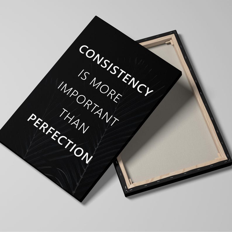 K&ouml;nnte beinhalten: Schwarzer Leinwanddruck mit dem wei&szlig;en Text &bdquo;CONSISTENCY IS MORE IMPORTANT THAN PERFECTION&ldquo;. Die Leinwand ist auf einen Holzrahmen gespannt. Der Hintergrund ist hellgrau.