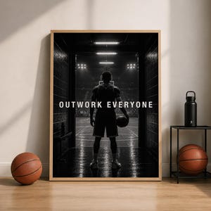 Könnte beinhalten: Ein gerahmter schwarz-weißer Wandkunstdruck, der einen Basketballspieler in einem Tunnel mit Blick auf ein Spielfeld zeigt, mit dem zentrierten Text OUTWORK EVERYONE. Der Druck wird mit zwei Basketbällen und einer schwarzen Trinkflasche präsentiert.