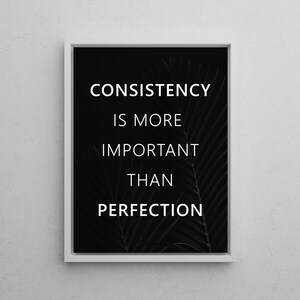 K&ouml;nnte beinhalten: Gerahmter Druck mit dem Text "CONSISTENCY IS MORE IMPORTANT THAN PERFECTION" in Wei&szlig; auf schwarzem Hintergrund. Der Druck hat einen wei&szlig;en Rand und ein subtiles Palmenblatt-Design.