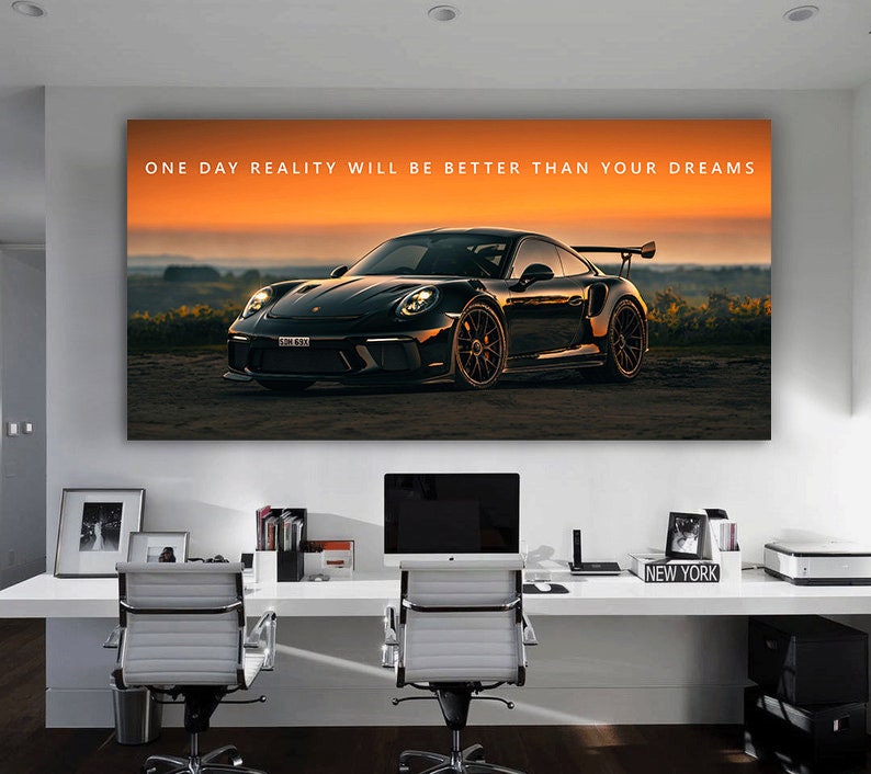 May include: A large canvas print featuring a black sports car set against a sunset backdrop. The text "ONE DAY REALITY WILL BE BETTER THAN YOUR DREAMS" is printed across the top. The print is displayed above a white desk with office chairs.