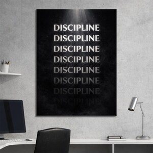 May include: A black and white wall art print with the word "DISCIPLINE" repeated multiple times in a vertical arrangement. The text is in a bold, sans-serif font, and the background has a textured appearance. The artwork is displayed in a modern office setting.