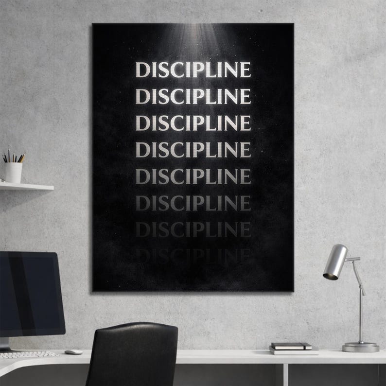 May include: A black and white wall art print with the word "DISCIPLINE" repeated multiple times in a vertical arrangement. The text is in a bold, sans-serif font, and the background has a textured appearance. The artwork is displayed in a modern office setting.