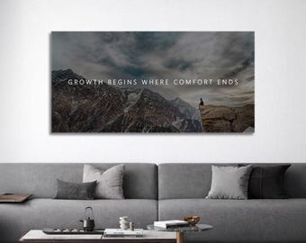 May include: A canvas print featuring a mountain landscape under a cloudy sky. The text "GROWTH BEGINS WHERE COMFORT ENDS" is displayed across the top. A person is silhouetted on a cliff, adding a sense of scale and perspective.