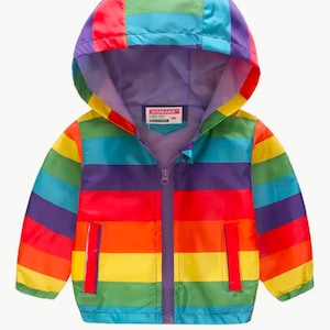 Può includere: Una giacca a righe arcobaleno colorata con cappuccio viola e chiusura a zip. La giacca ha un'etichetta che dice "JOMAK".