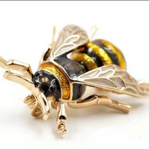 May include: A gold-toned bee brooch with black and yellow enamel detailing. The bee has detailed wings and legs.