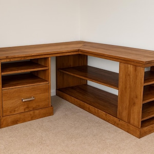 以下が含まれることがあります： 温かみのある茶色の仕上げが施されたL字型の木製デスク。デスクには、シルバーの取っ手が付いた引き出しと、収納用のオープンシェルフが付いています。コーナーデザインは、ホームオフィスやワークスペースのスペースを最大化するのに最適です。
