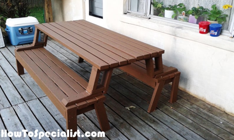 Pu&ograve; includere: Un tavolo da picnic in legno marrone con panche attaccate. Il tavolo ha un piano a doghe ed &egrave; progettato per l'uso all'aperto. Le panche sono collegate al telaio del tavolo. Il tavolo &egrave; su un ponte di legno.