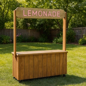 Può includere: Un chiosco di limonata in legno con un cartello con la scritta "LEMONADE" in lettere rosa. Il chiosco è realizzato in legno marrone chiaro e ha un bancone e un'area di stoccaggio inferiore. È allestito su un prato.