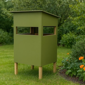 Puede incluir: Un puesto de caza de madera verde con forma rectangular y techo plano. Tiene aberturas rectangulares en la parte delantera y los lados. El puesto está elevado sobre cuatro patas de madera en un jardín.