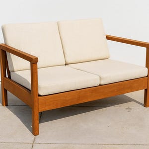 以下が含まれることがあります： 天然木仕上げの2人掛け木製ソファ。クリーム色のクッションとアームレストが2つ付いています。フレームは木製で、シンプルでモダンなデザインです。屋内または屋外での使用に適しています。