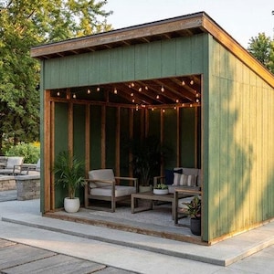 Könnte beinhalten: Außenbereich mit einer grünen, schuppenartigen Struktur mit Holzrahmen und Lichterketten. Im Inneren befinden sich zwei graue Sessel, ein Couchtisch und Topfpflanzen. Eine Beton-Terrasse führt zu einer Feuerstelle aus Stein und Sitzgelegenheiten.