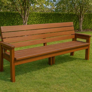 Op de afbeelding: Een bruine houten bank met een lattenrug en zitting, en armleuningen. De bank staat op een groen gazon, met bomen en een haag op de achtergrond. De bank is ongeveer 152 cm lang.