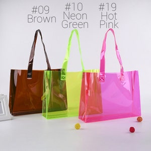 May include: Three clear plastic tote bags with handles. The bags are brown, neon green, and hot pink.