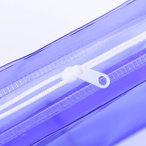 May include: Close-up of a clear purple zippered pouch with a white zipper pull.