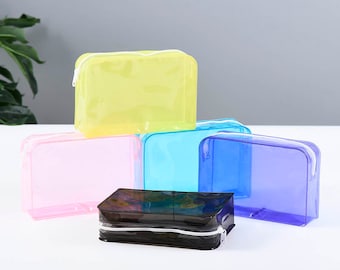 May include: Five clear plastic zippered pouches in different colors: yellow, pink, light blue, dark blue, and black. The pouches are stacked on top of each other.
