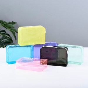May include: Six clear plastic zippered pouches in different colors: light blue, pink, purple, black, light green, and yellow. The pouches are stacked on top of each other.