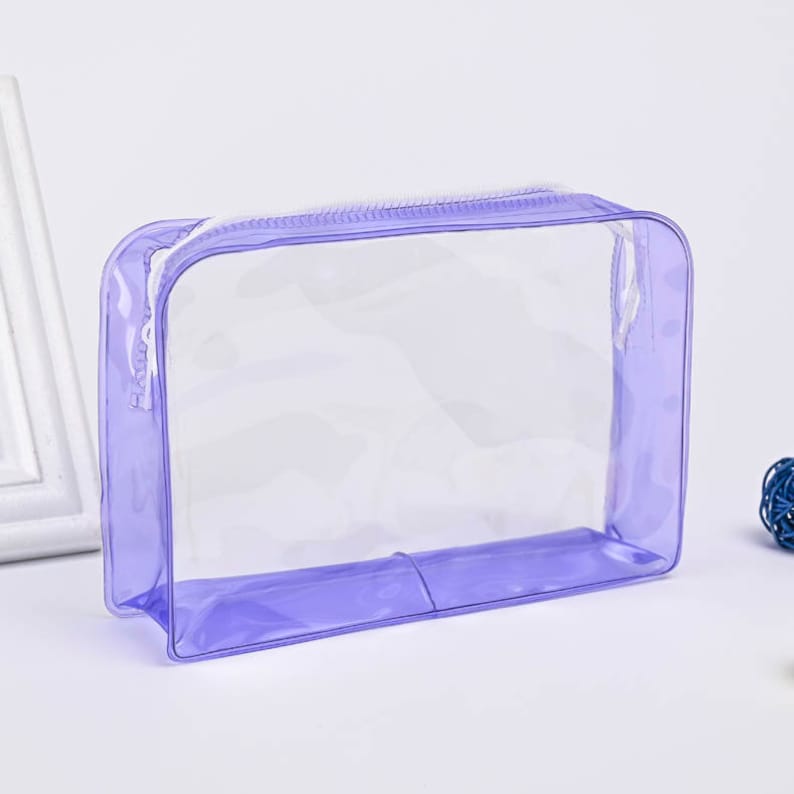 May include: A clear, lavender-colored zippered pouch with a white zipper. The pouch is made of a flexible, waterproof material.