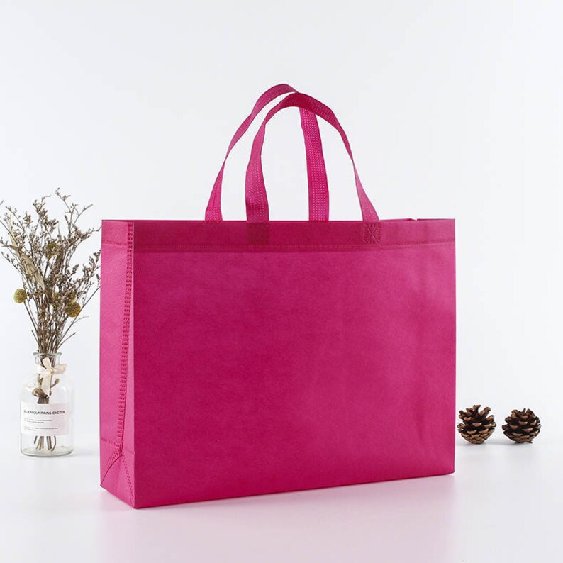 May include: A bright pink reusable shopping bag with two handles. The bag is made of non-woven fabric and has a flat bottom.