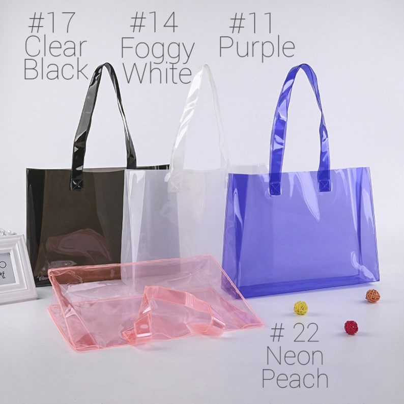 May include: Four clear plastic tote bags with handles. The bags are in the colors black, white, purple, and pink. The bags are labeled with numbers and colors: #17 Clear Black, #14 Foggy White, #11 Purple, and #22 Neon Peach.