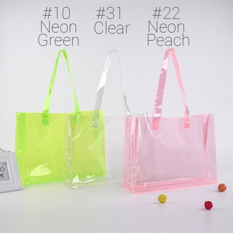May include: Three clear plastic tote bags with handles. The bags are in different colors: neon green, clear, and neon peach. The bags are labeled with numbers and colors: #10 Neon Green, #31 Clear, and #22 Neon Peach.