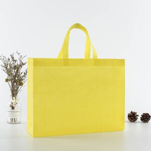 May include: A bright yellow reusable shopping bag with two handles. The bag is made of non-woven fabric and is a great alternative to plastic bags.