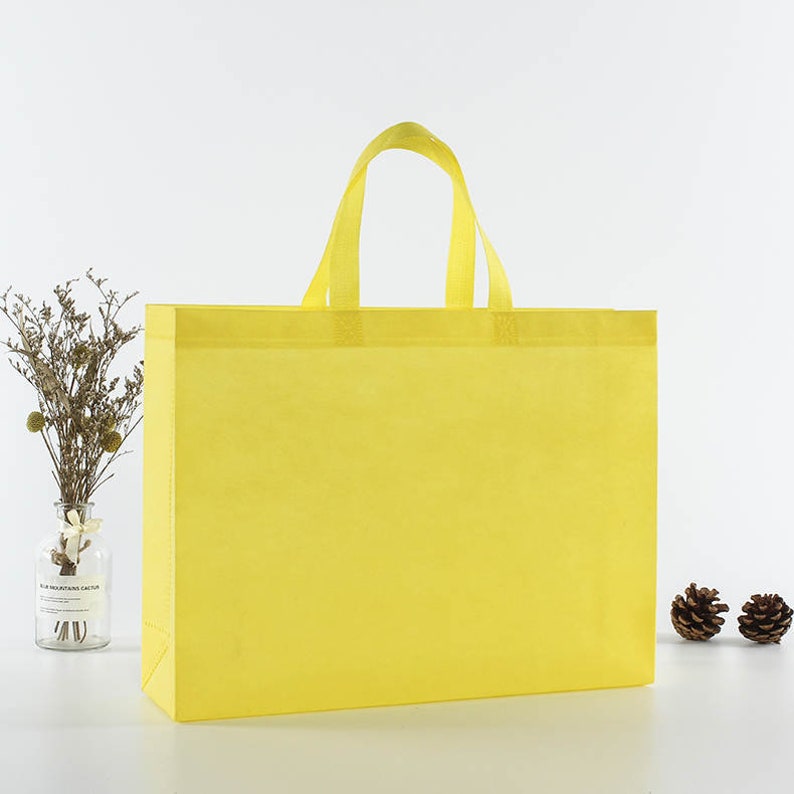May include: A bright yellow reusable shopping bag with two handles. The bag is made of non-woven fabric and is a great alternative to plastic bags.