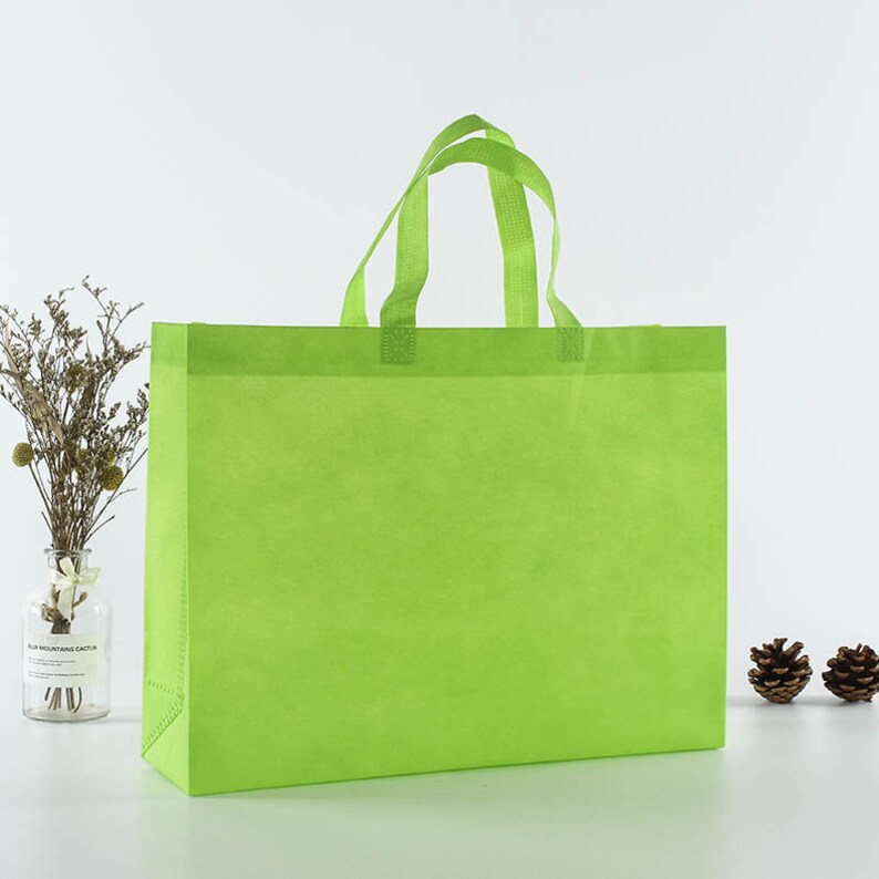 May include: A bright green reusable shopping bag with two handles. The bag is made of non-woven fabric and is a great alternative to plastic bags.